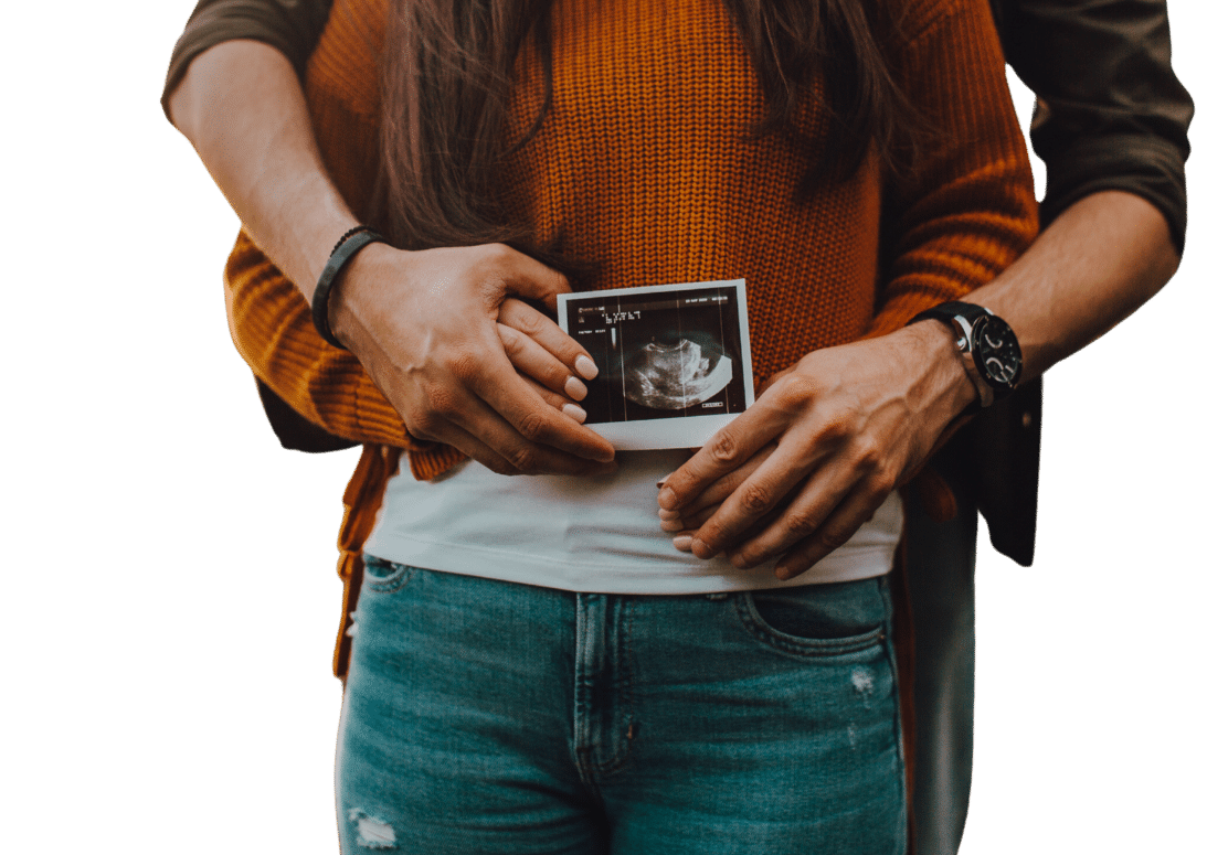 Zwei Menschen stehen hintereinander und halte auf Bauchhöhe ein Ultraschallbild eines Babys.